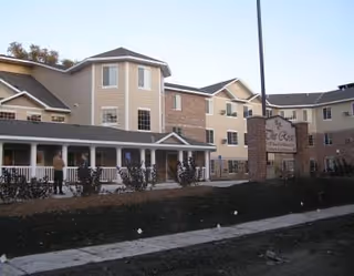 Exterior view of Rose of East Des Moines senior living facility with a sign and walkway