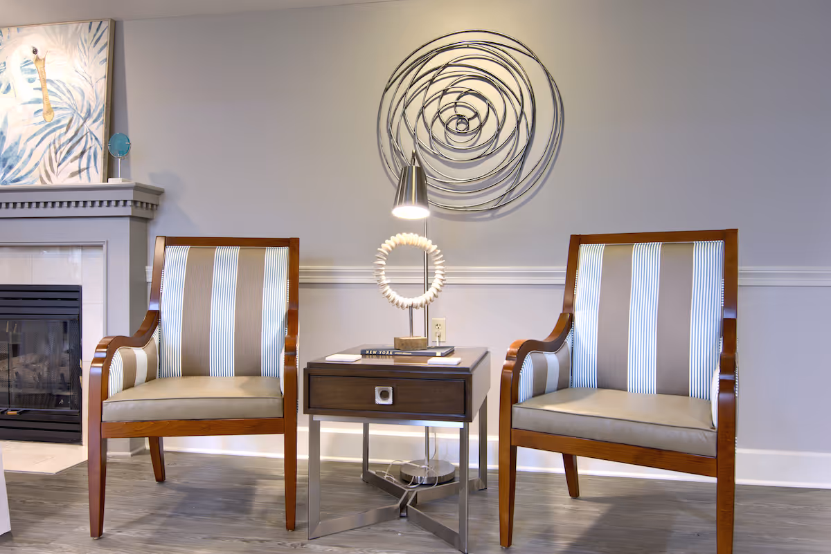 Two striped armchairs flank a side table with a lamp and decorative wall art in a seating area.