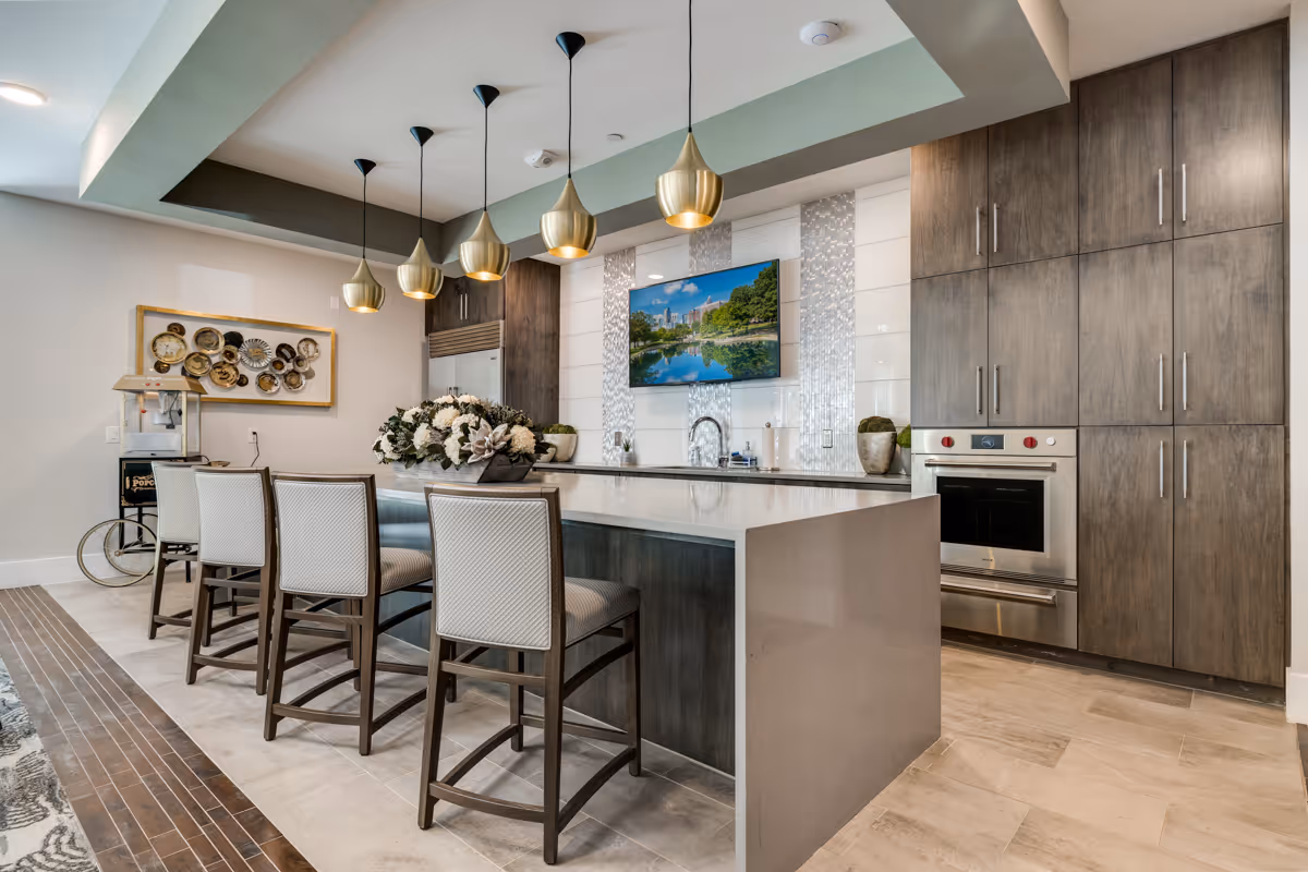Modern communal kitchen with a large island, four bar stools, pendant lights, built-in oven and wood cabinets.