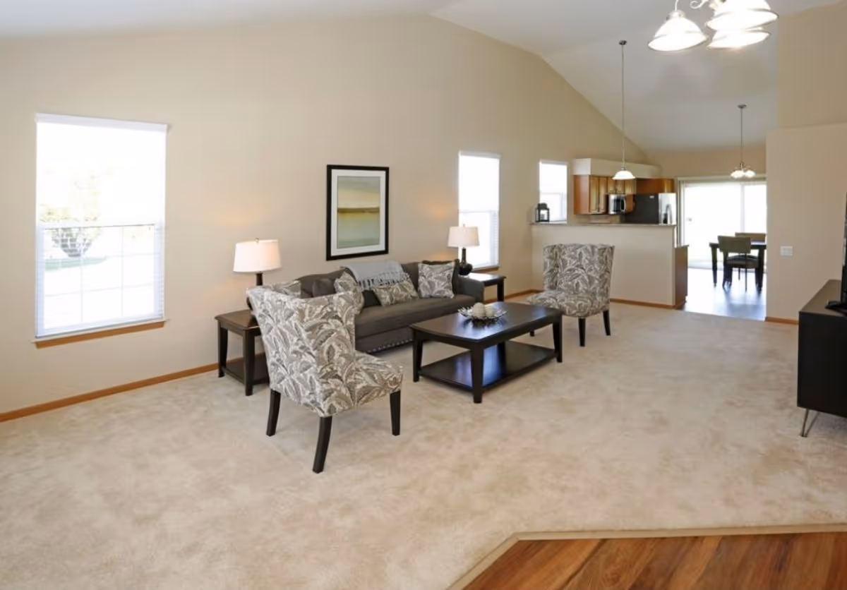 Spacious furnished living room with a sofa, patterned armchairs, coffee table and an open view into the kitchen and dining area.