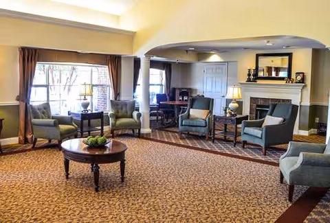 Spacious senior living room with armchairs, coffee table, lamps, fireplace, and large windows.