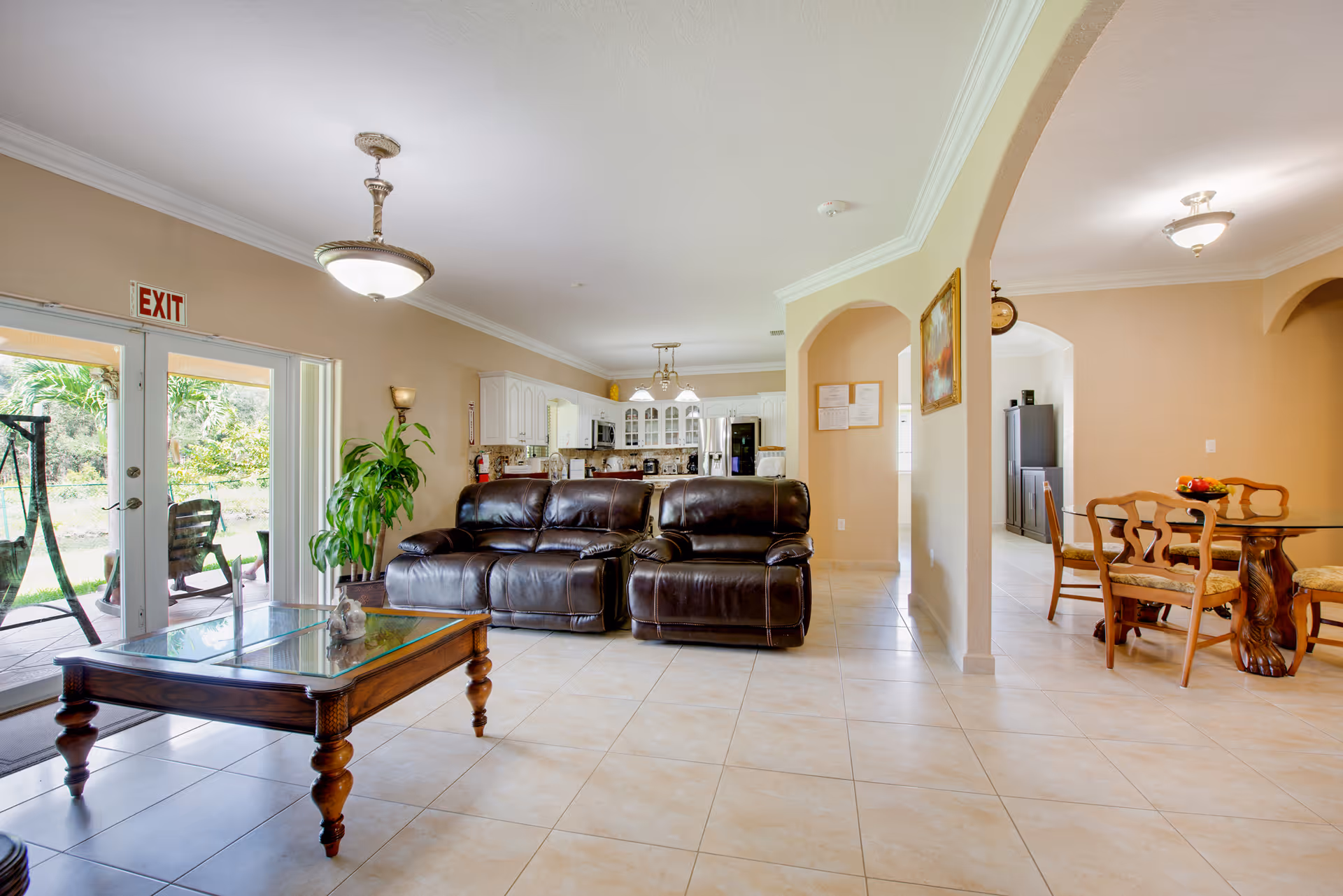 Bright open living area with a dark leather sofa and glass coffee table, kitchen visible in the background and a dining table to the right.