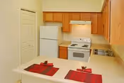 Small kitchen with white refrigerator, electric stove, wooden cabinets and a countertop set with two red placemats.