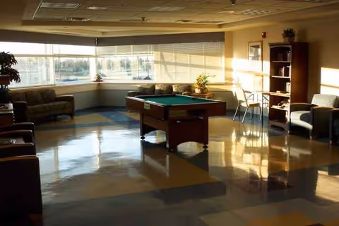 Bright senior living lounge with a pool table, seating, and large windows.