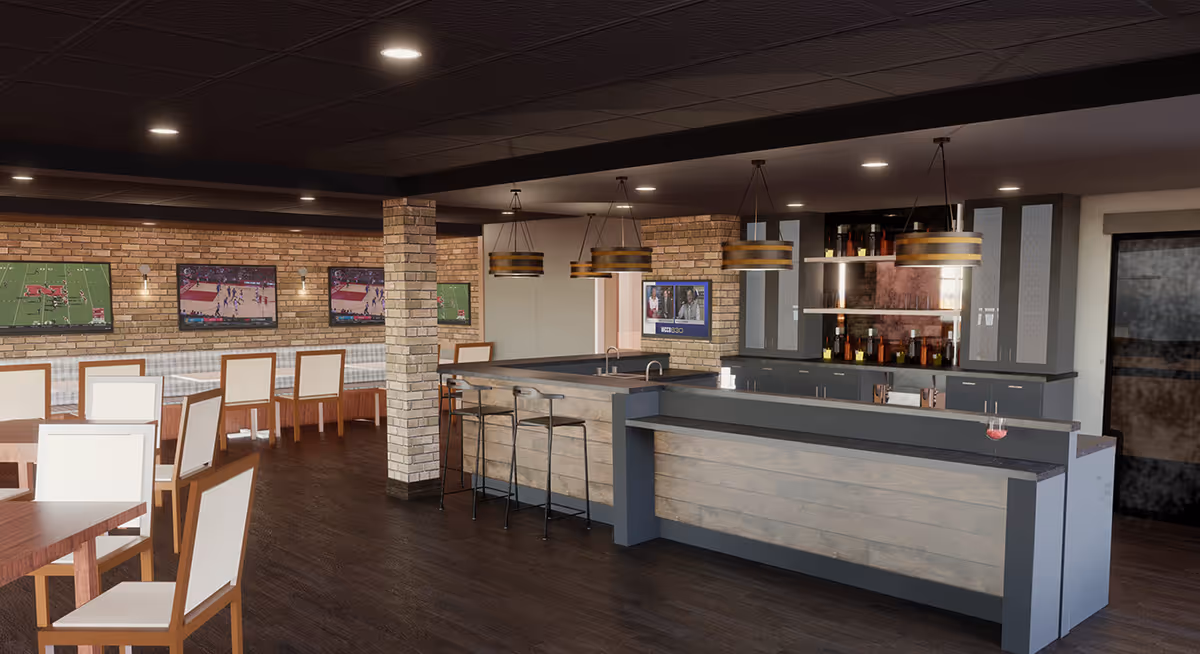 Interior view of a modern common area with a bar counter featuring three bar stools, pendant lights, and a back cabinet stocked with bottles. There are multiple tables and chairs arranged for seating, and several flat-screen TVs mounted on a brick wall showing sports and news channels.
