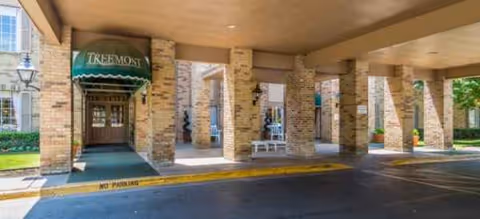 Brick building entrance with columns, a green awning, and benches under a covered driveway.