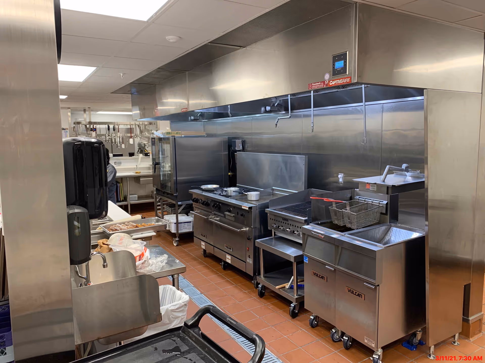 Stainless-steel commercial kitchen with range, deep fryers, prep sinks and shelving.