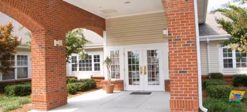 Brick arch entrance with glass doors, potted plants, and manicured shrubs at Brookdale Wilmington