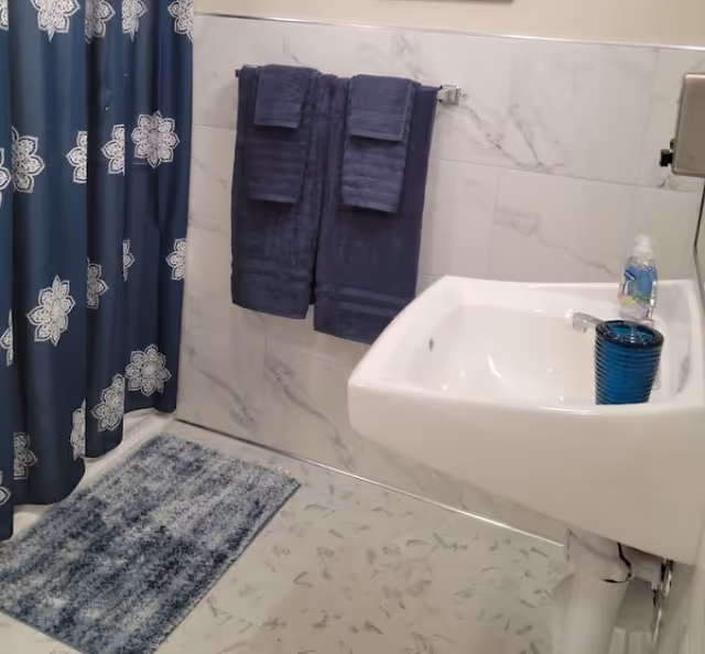 Blue towels hang by a marble-tiled bathroom sink and blue shower curtain.