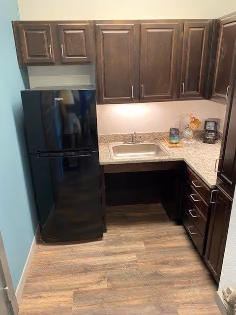 Small kitchenette with dark wood cabinets, a black refrigerator, a countertop sink and a coffee maker.