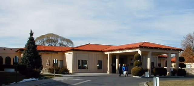 Front entrance of a single-story care center with a covered porte-cochere and two people walking toward the doors.