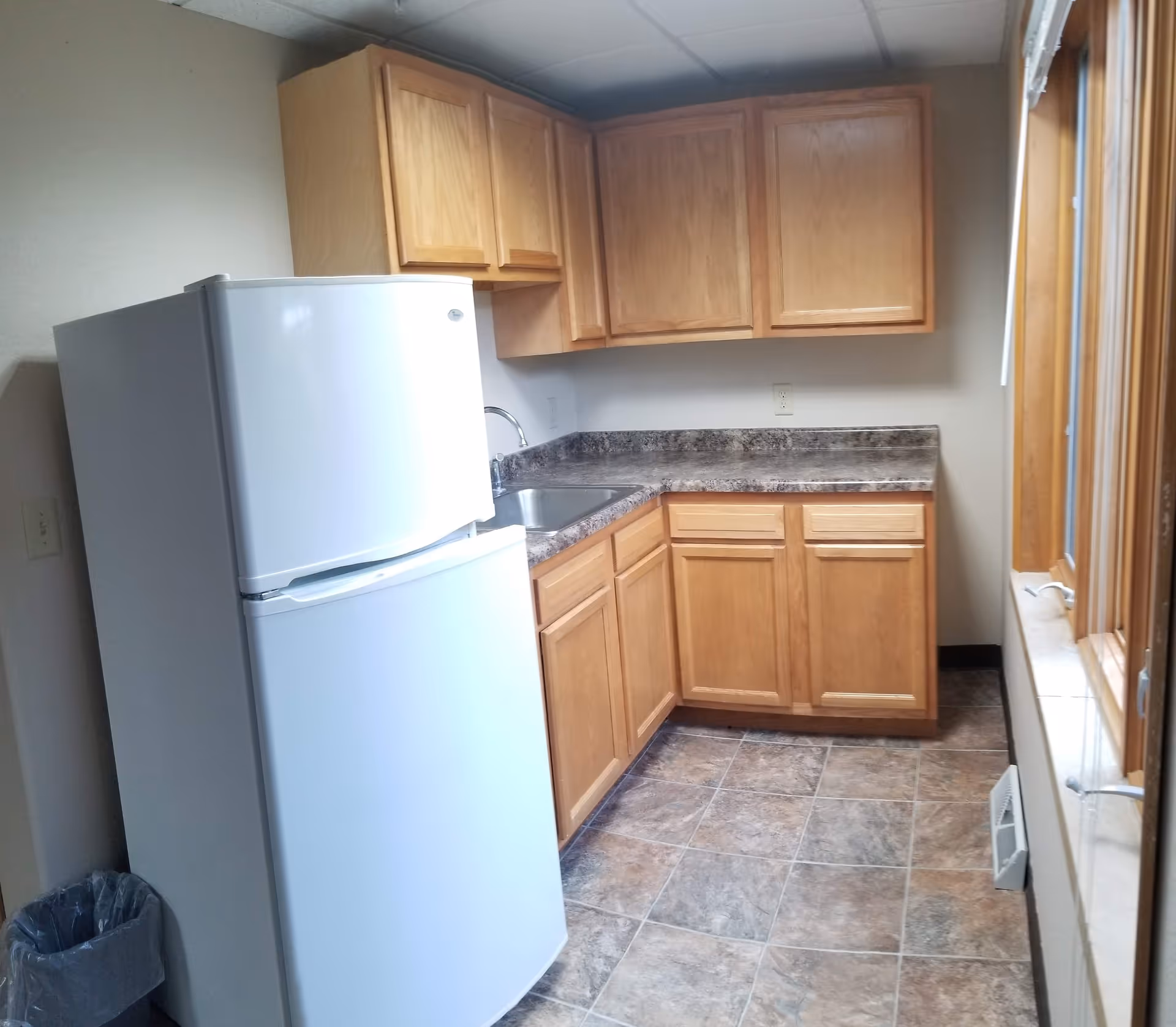 Small kitchenette with a white refrigerator, wooden cabinets, a sink and laminate countertops over a tiled floor.