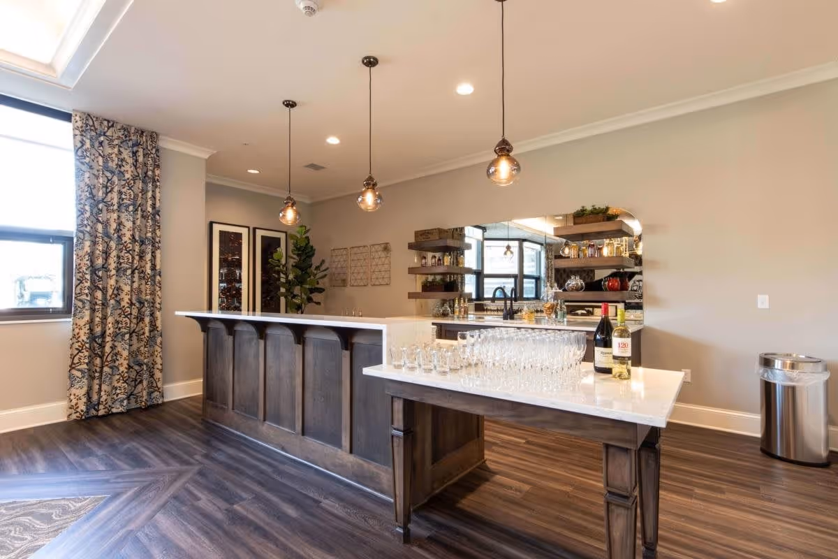 Modern communal bar area with a marble-topped island, pendant lights, glassware and bottles in a lounge-like kitchen space.