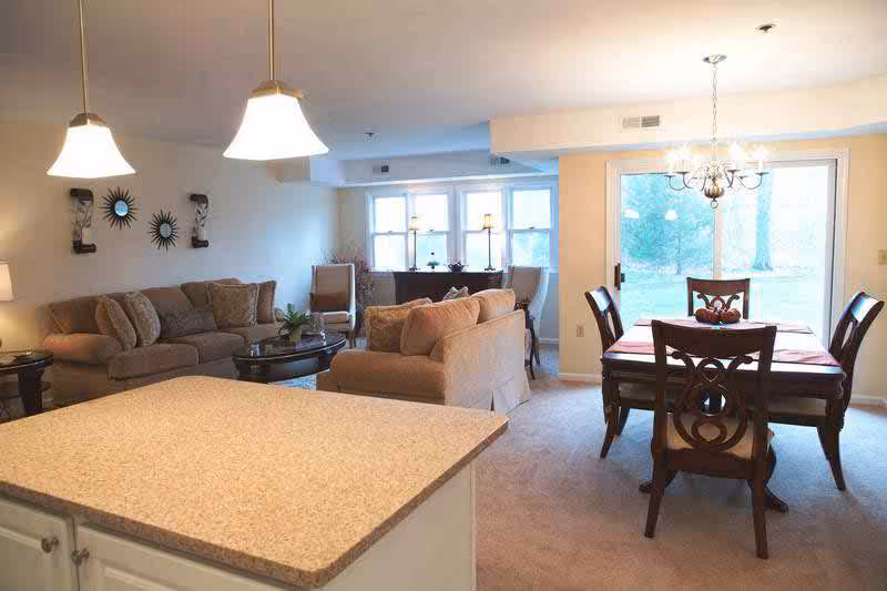 Open-plan interior with a kitchen island in the foreground, a sofa seating area and a dining table by sliding glass doors.