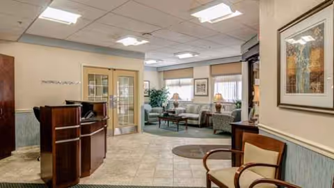 Lobby reception area with seating, desk, glass doors, lamps, and framed art.