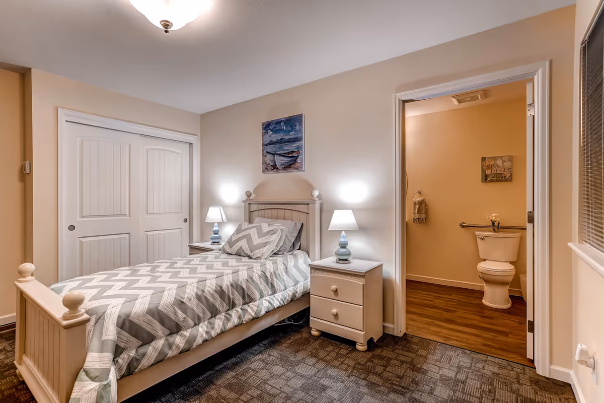 Single bed with chevron-patterned bedding, two nightstands, lamps, and an adjacent bathroom doorway.