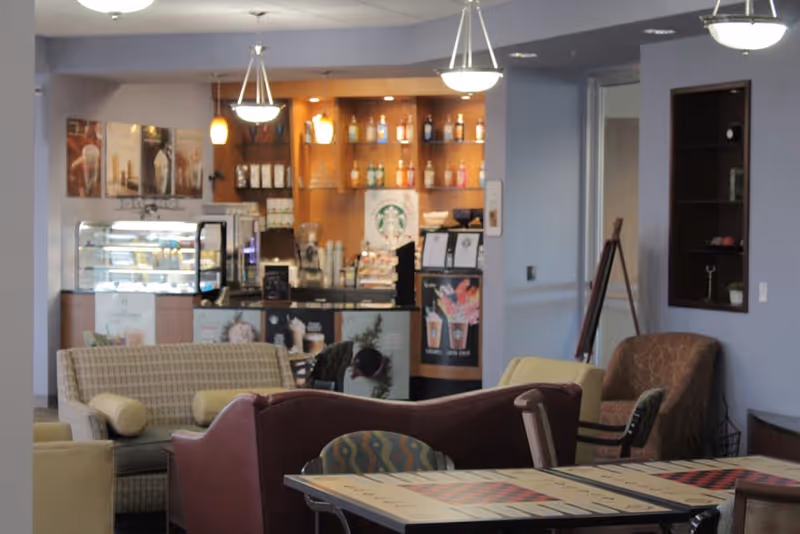 Lounge with sofas and tables in front of a small coffee bar and display case bearing a Starbucks logo.