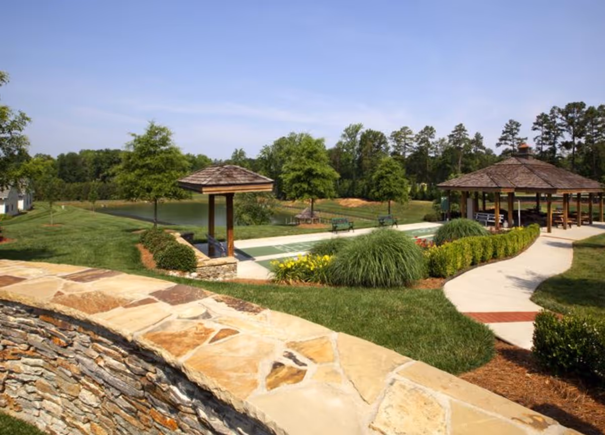 Landscaped outdoor area with a stone wall, walking paths, gazebos, benches, and a pond.