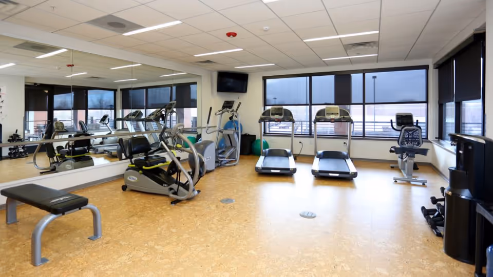 Bright fitness room with treadmills, exercise bikes, a weight bench, and mirrored wall.