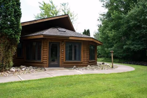 Wooden cabin-style senior living facility exterior with curved path and greenery.