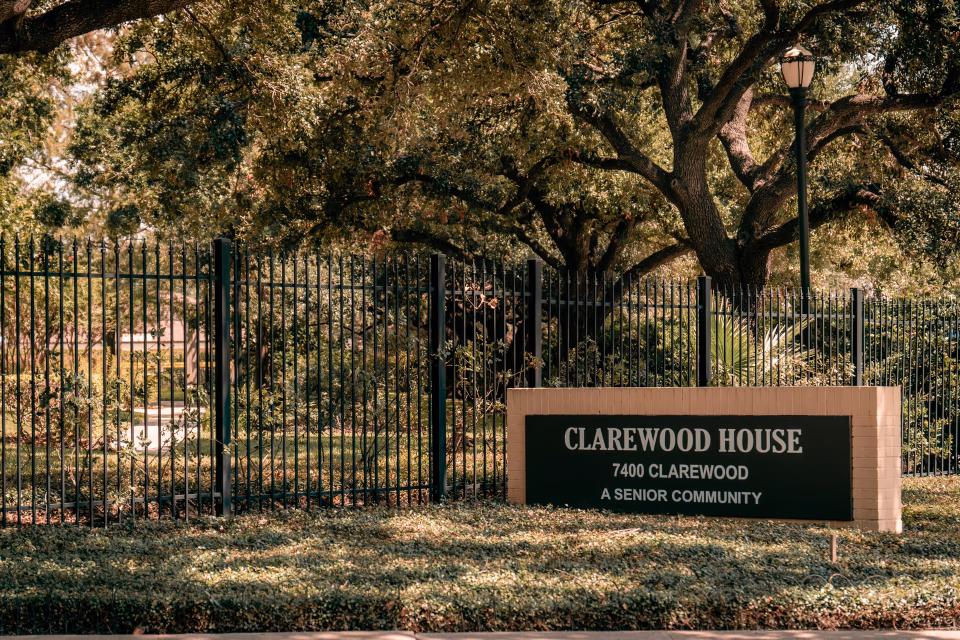 Outdoor view of Clarewood House senior community entrance sign with a black metal fence and large trees in the background.