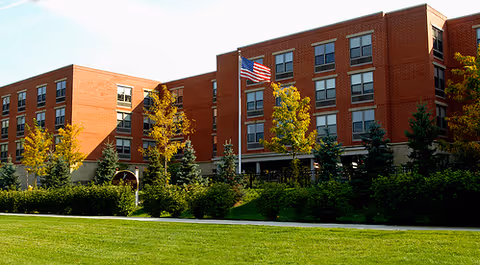 Front exterior view of a brick senior living facility with trees and an American flag.