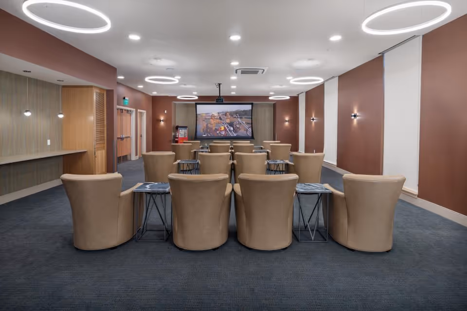 Beige lounge chairs arranged in rows facing a large projection screen in a modern community media room.