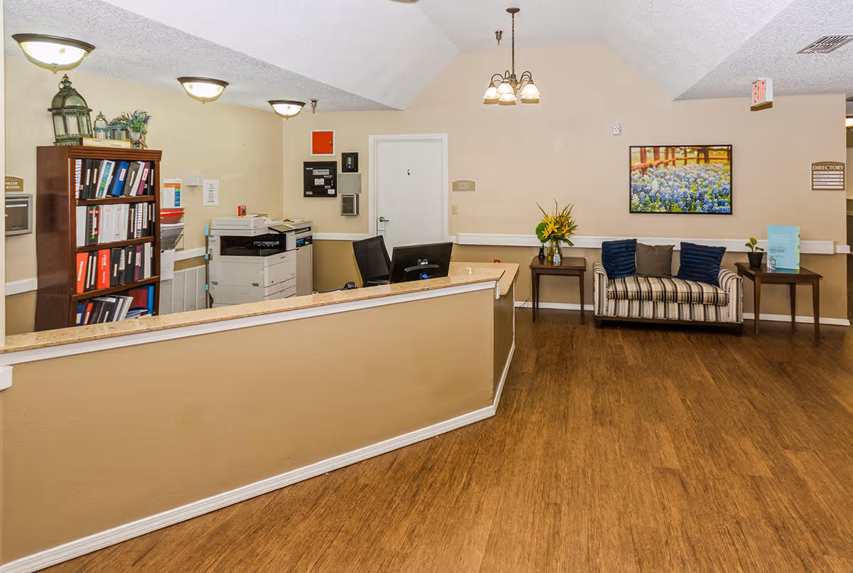 Reception desk and seating area with a striped couch, side tables, bookshelf, and office equipment in a facility lobby.