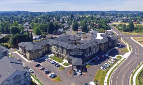 Aerial view of a large senior living complex with multiple connected buildings, parking areas, landscaped grounds, and surrounding neighborhood.