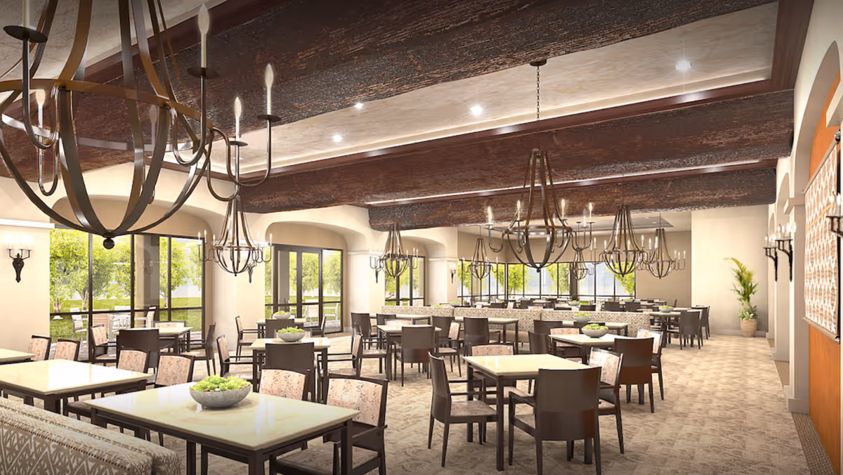 Large elegant dining room with numerous tables, pendant chandeliers, and windows showing greenery outside.