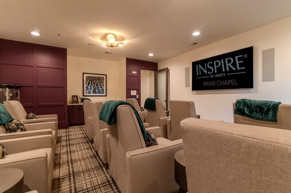 Small cozy media room with rows of beige reclining chairs facing a wall-mounted screen reading "INSPIRE BRIAR CHAPEL".