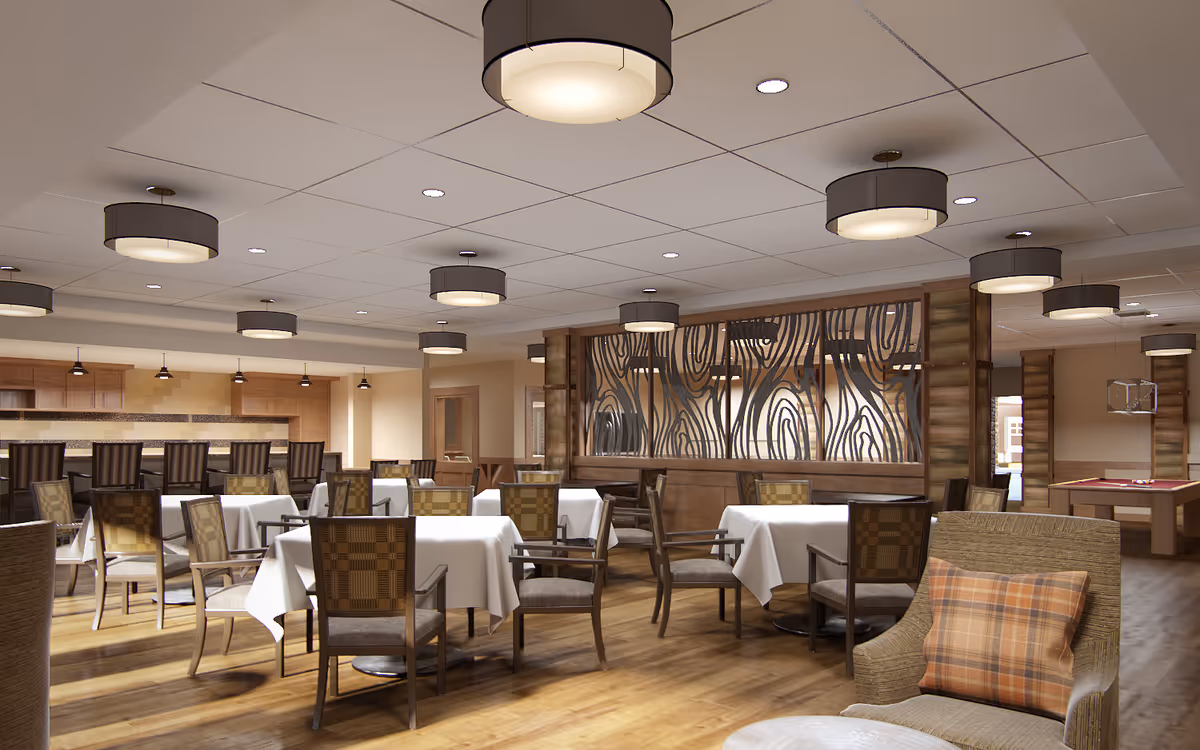 A spacious dining area with multiple tables covered in white tablecloths and surrounded by wooden chairs with patterned cushions. The room features wooden flooring, modern ceiling lights, and a decorative wooden partition with an abstract design. In the background, there is a bar area with high chairs and a kitchen counter, and to the right, a pool table is partially visible.