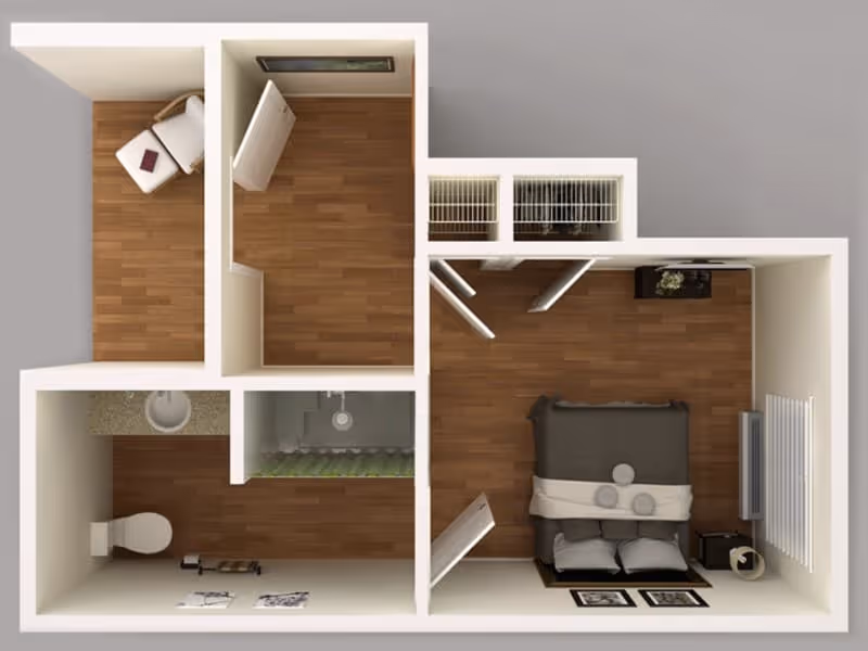 Top-down view of a small apartment floor plan showing a bedroom with a bed, nightstand, and dresser; a bathroom with a toilet, sink, and shower; and a small separate room with a chair and a book on it. The floors are wooden and the walls are light-colored.