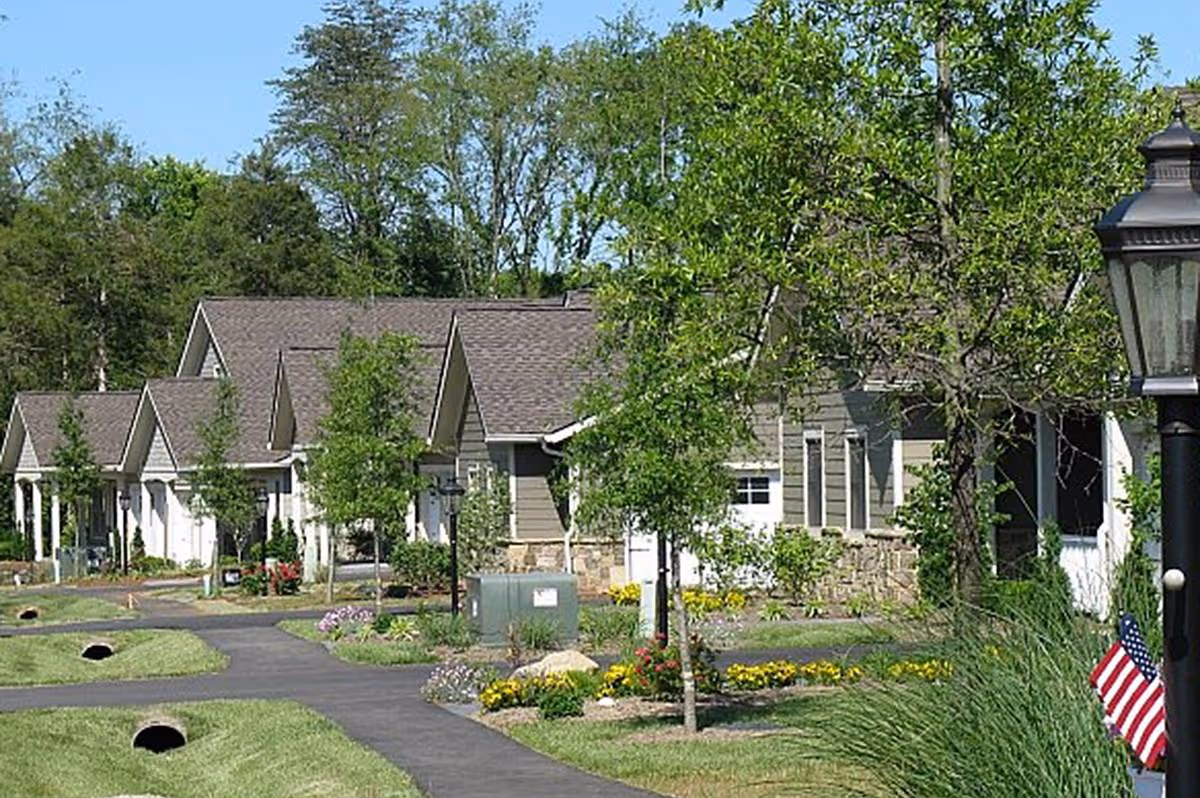 Row of single-story cottage-style residences with lawns, walkways, trees and landscaping at a senior living community.