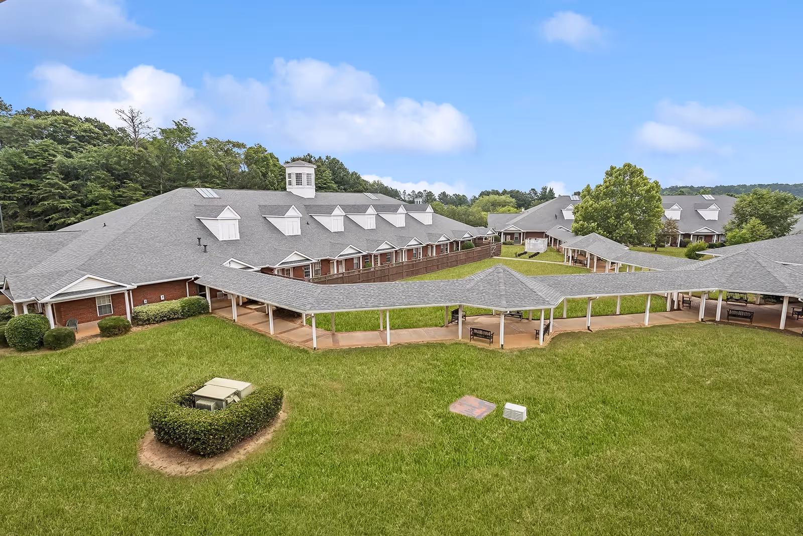 Aerial view of a senior living facility courtyard with connected brick buildings, covered walkways, and a large grassy lawn.