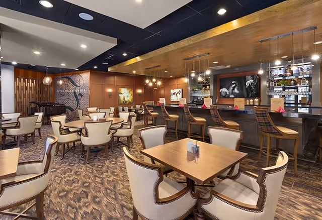 Spacious upscale dining room with wooden tables, upholstered chairs, and a bar with high stools.