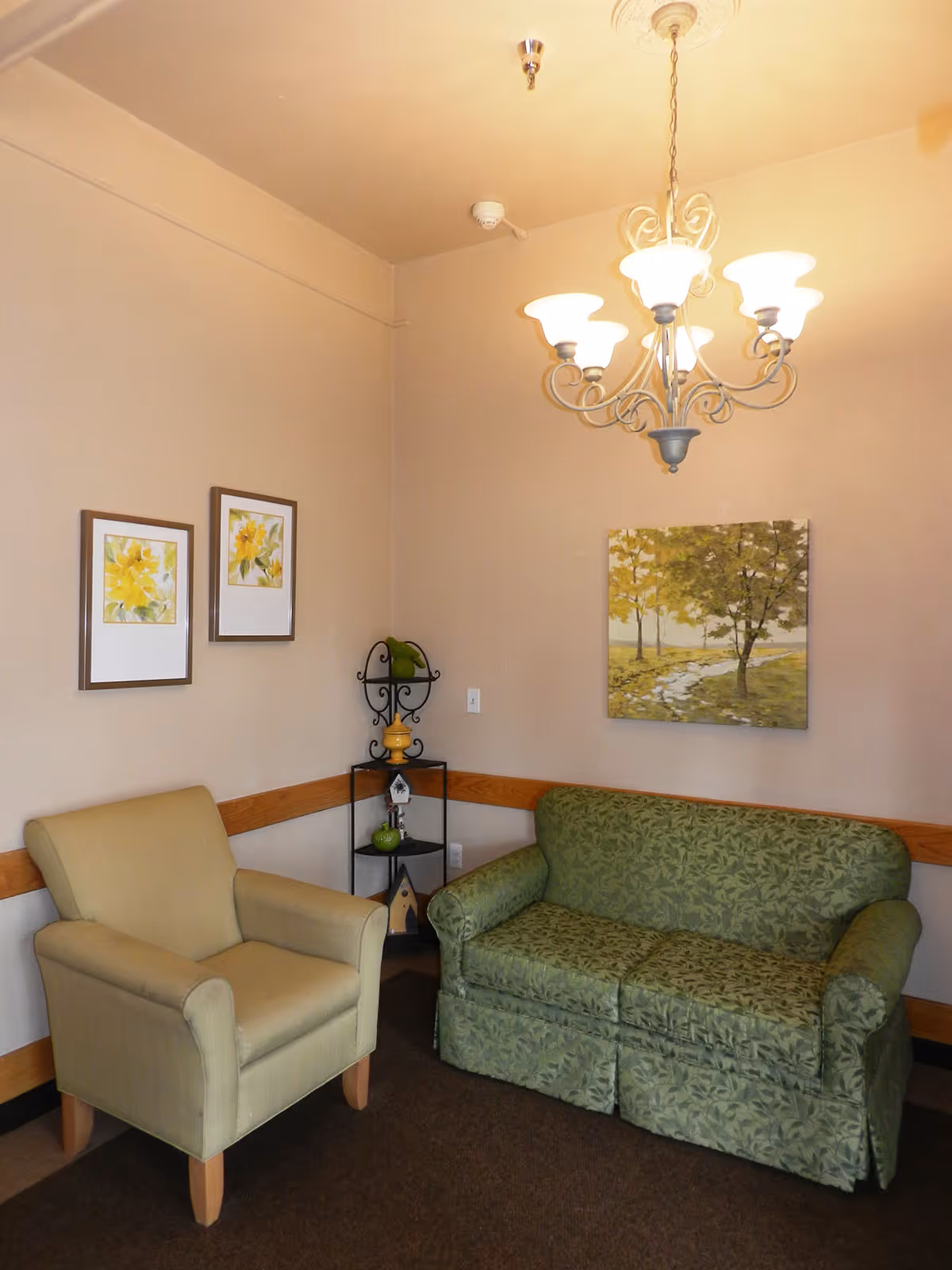 Small sitting area with a green patterned loveseat, beige armchair, wall art, and an overhead chandelier.