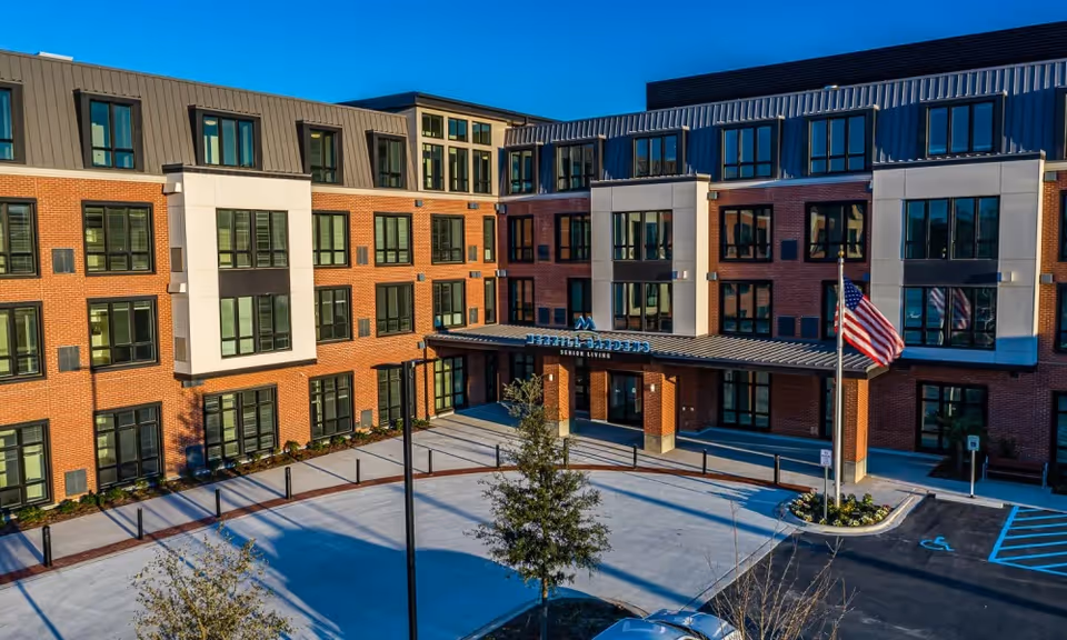 Front exterior of a multi-story brick senior living building with a covered entrance and an American flag.