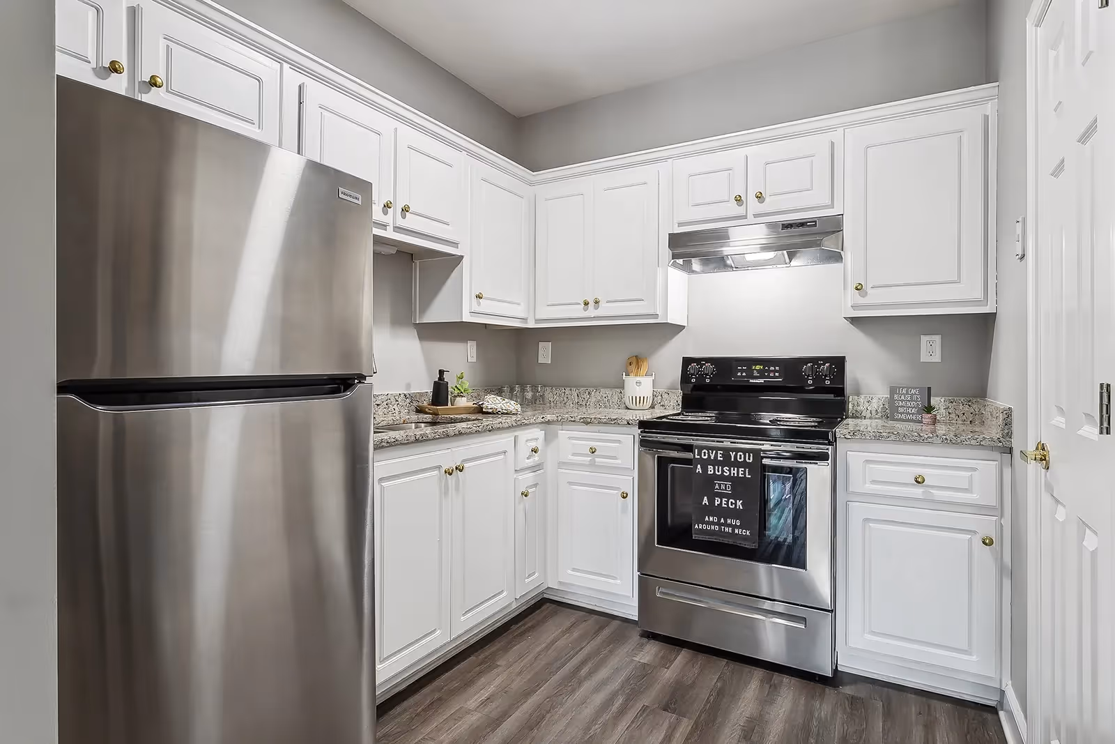 Modern kitchen with stainless steel refrigerator and stove, white cabinets, granite countertops, and wood-look flooring.