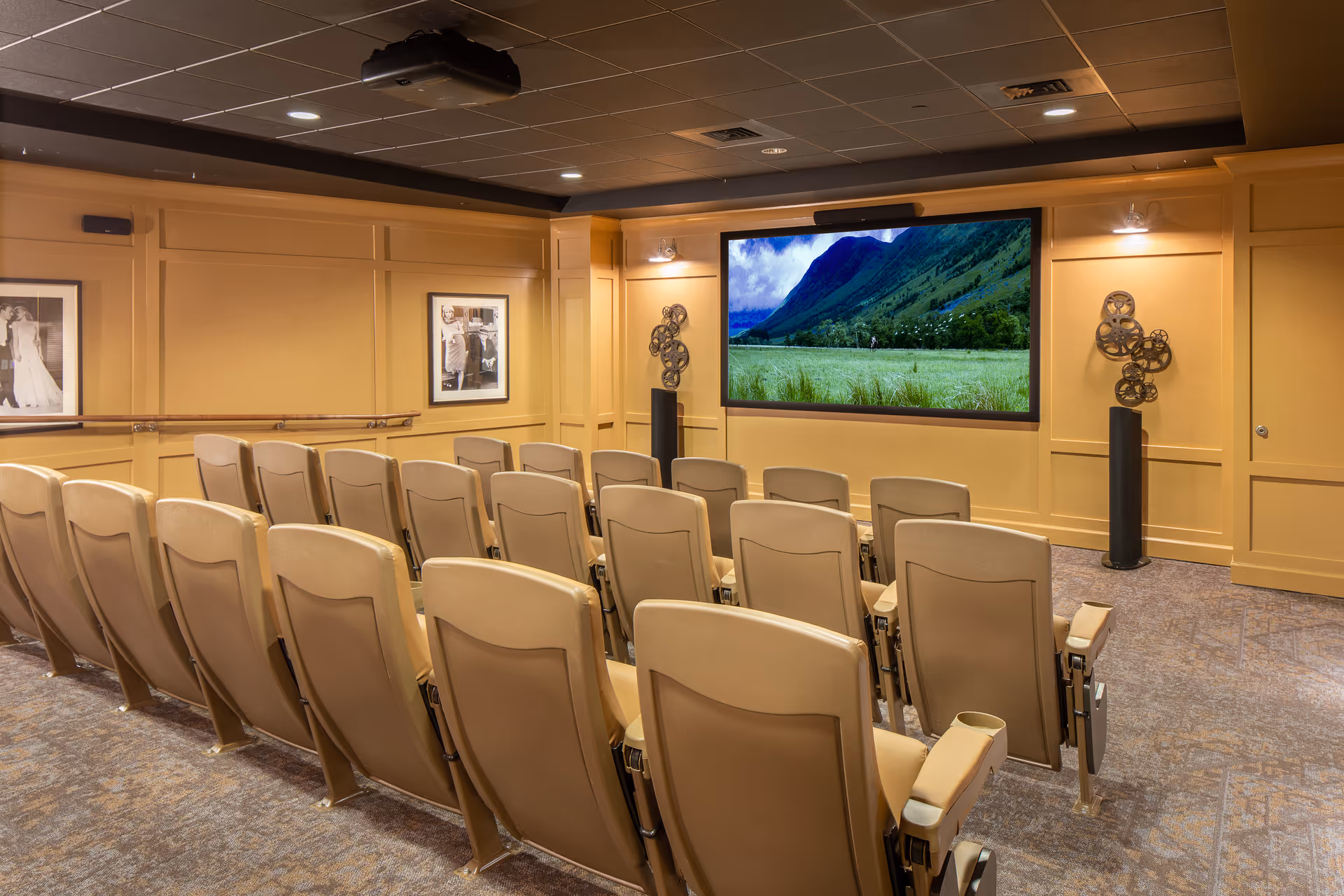 Small private screening room with rows of beige theater seats facing a large wall-mounted screen showing a mountain scene.
