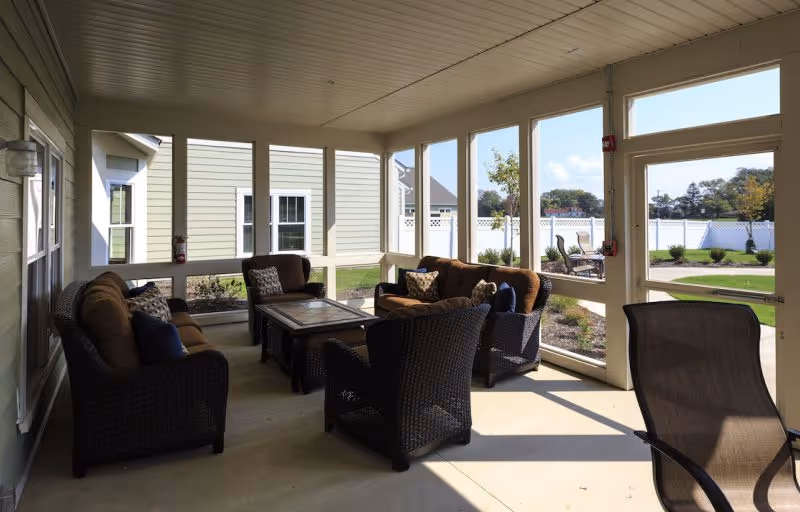 Covered screened porch with wicker sofas and chairs arranged around a central coffee table overlooking a landscaped yard.