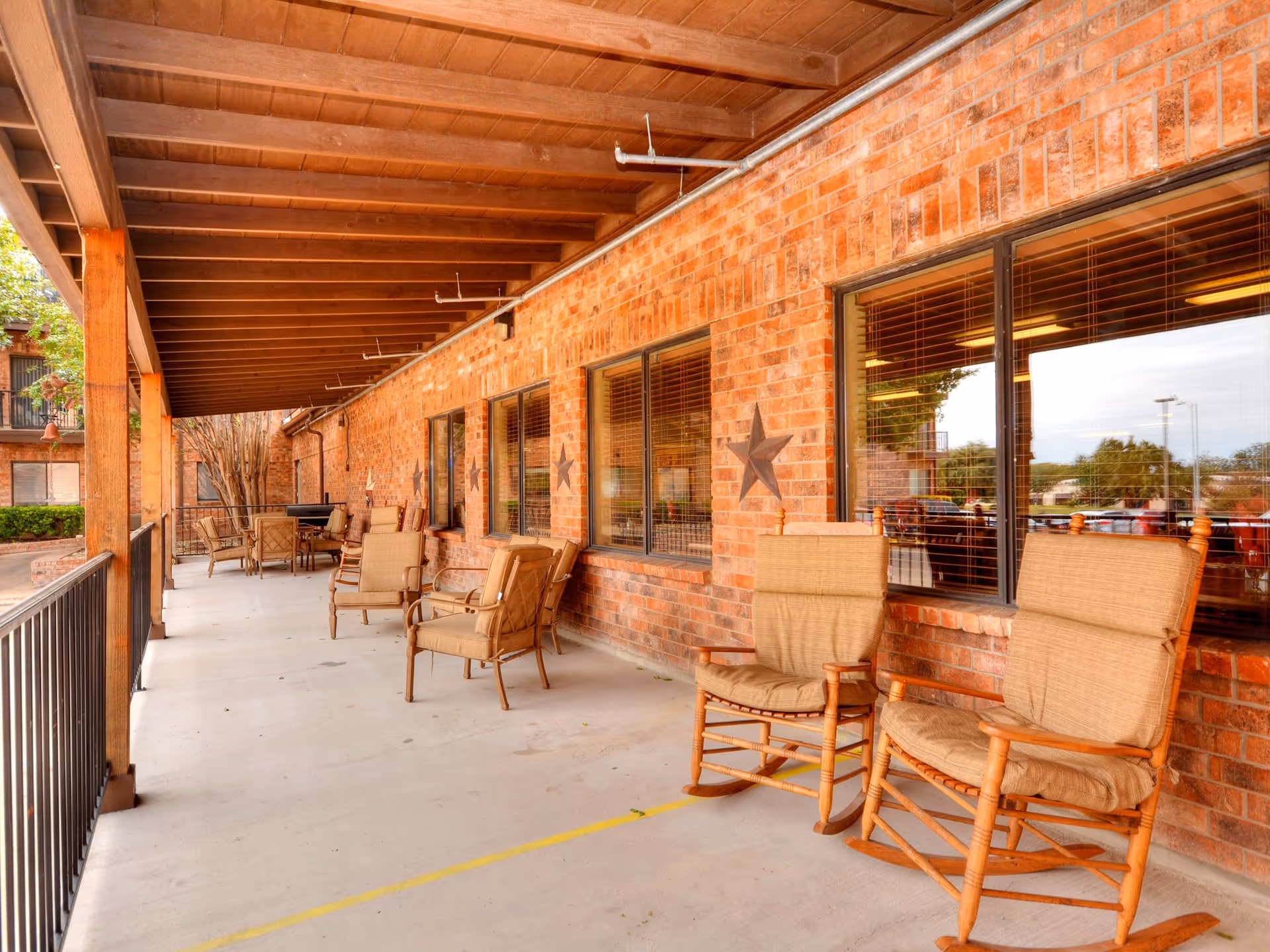 Covered brick patio with cushioned rocking chairs and seating along windows.