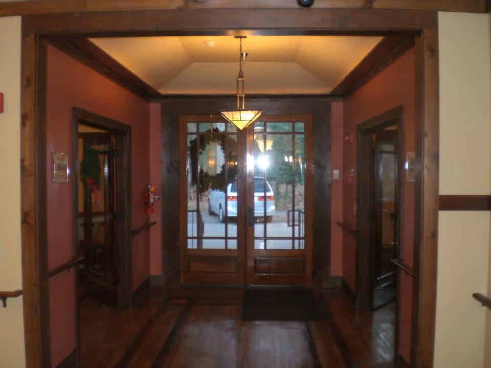Interior view of a wood‑trimmed entry hallway with double glass front doors and a white van visible outside.