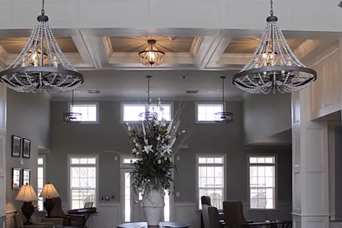 A bright, elegant communal lounge with high coffered ceilings, crystal chandeliers, seating areas and a large floral centerpiece.