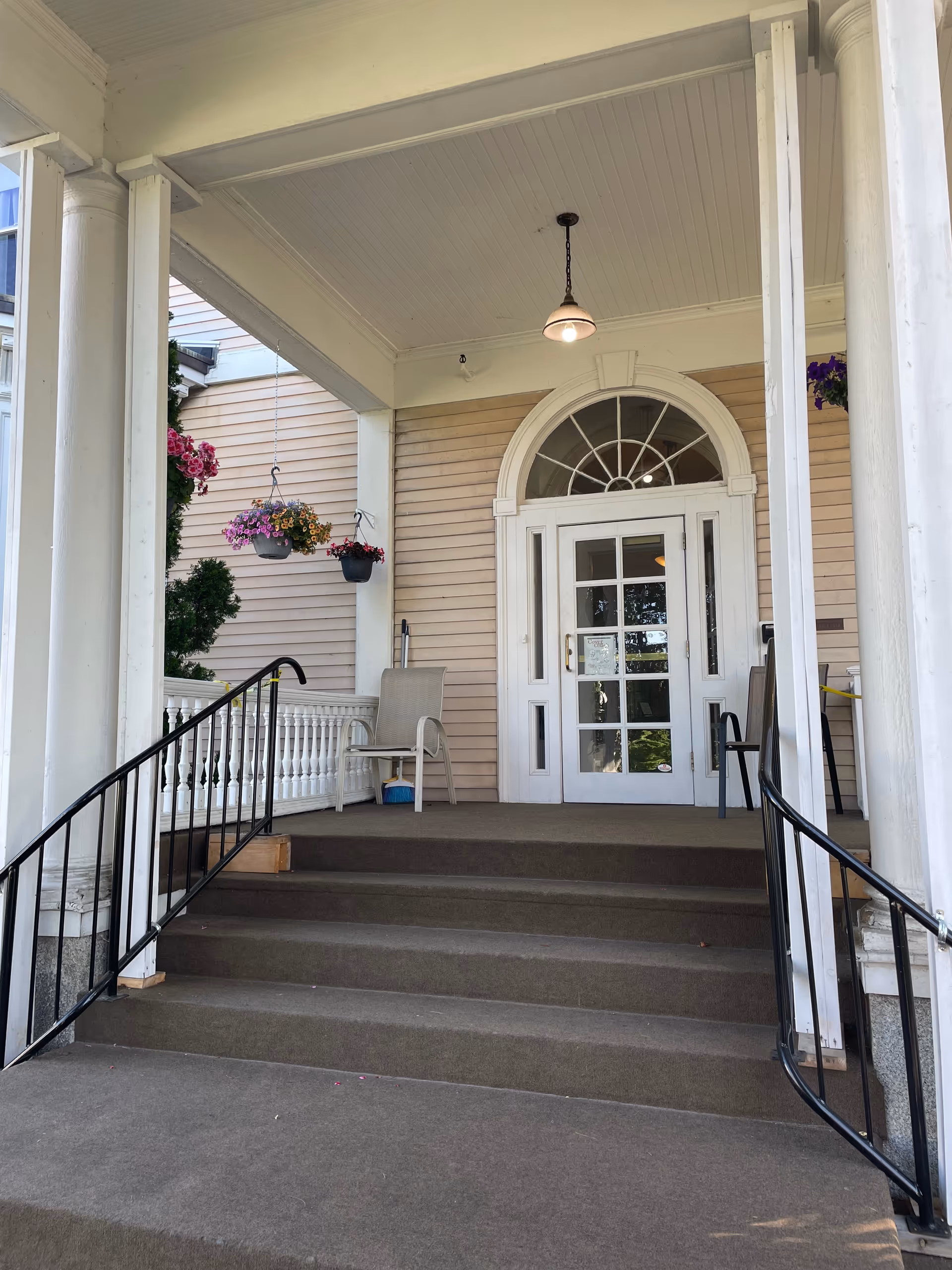 Carpeted front steps leading up to a covered porch and white glass-paneled entrance door with hanging flower baskets.
