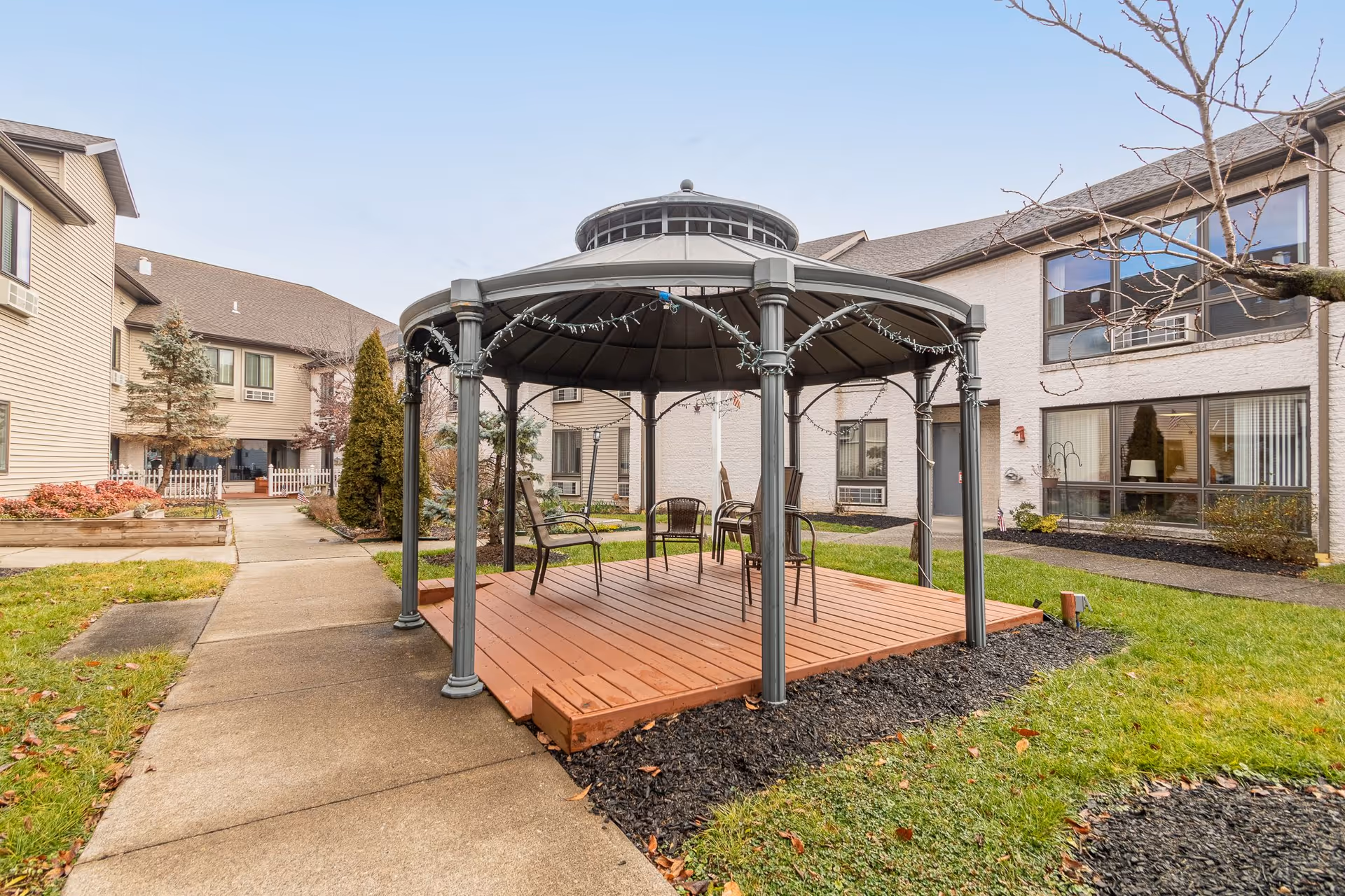 A courtyard with a covered gazebo and chairs between two wings of a senior living facility.