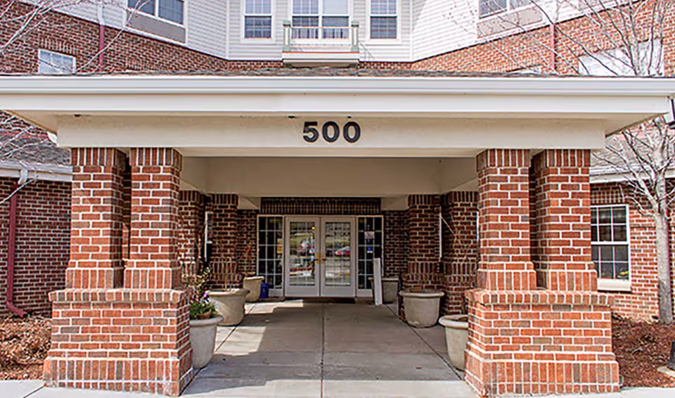 Entrance of a brick building with the number 500 displayed above the covered entryway supported by brick columns. There are large planters on either side of the walkway leading to glass double doors.
