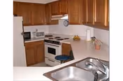 Compact kitchen with wooden cabinets, white countertops and appliances and a stainless steel sink in the foreground.