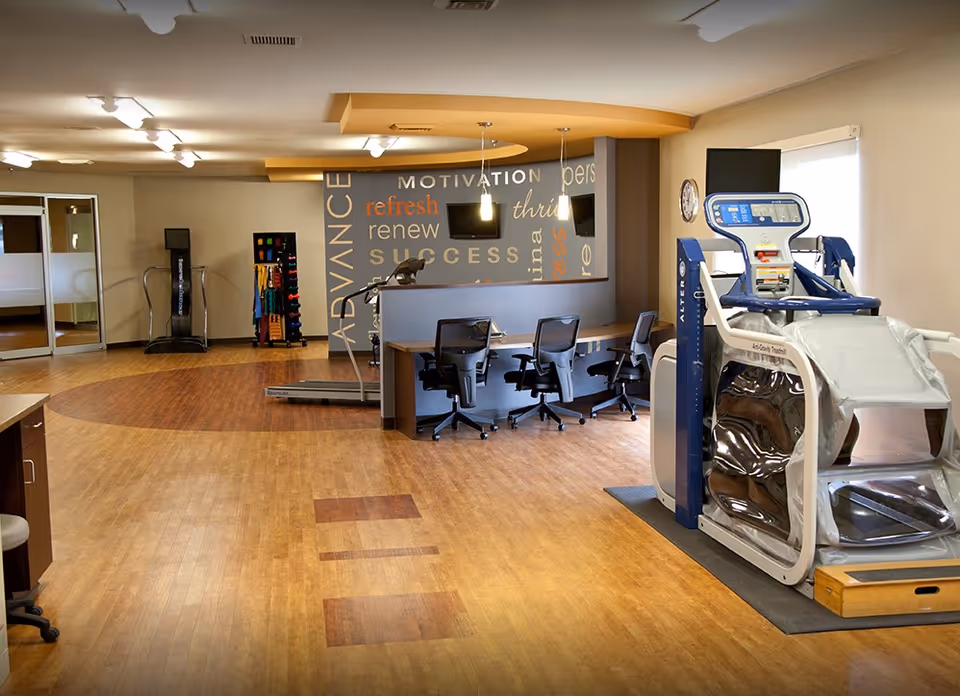 Spacious rehabilitation gym/interior with exercise machines, a desk with chairs, and a motivational word wall.