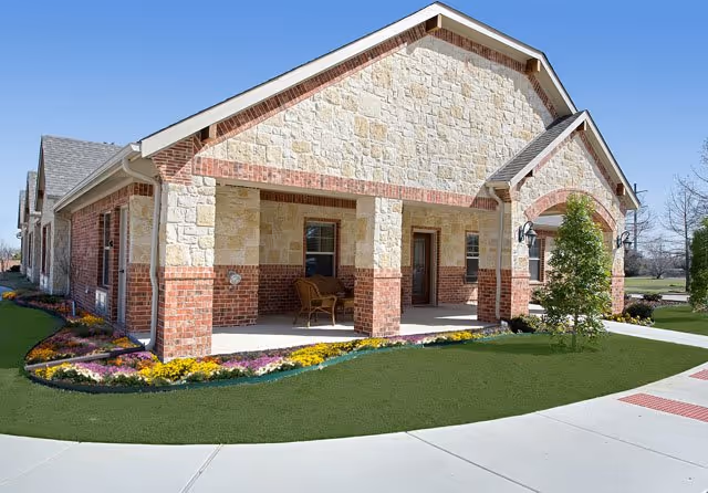 Front view of a stone-and-brick senior living building with a porch and landscaped grounds.